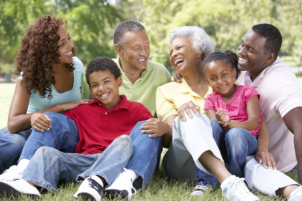 smiling family sitting on the ground with grandparents, parents and two children
